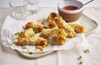 Krokante kaaskroketten liggen op een dienchaaltje, met een dipsausje in een zelfgedraaid keremakiekpotje. Er staan twee glaasjes water naast en de sticks zijn afgewerkt met verse oregano.