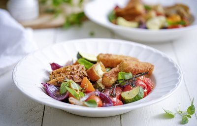 Een heerlijk en rijkgevuld slaatje is geserveerd in een diep wit bord. De kleurtjes van de basilicum, tomaten, rode ui en courgette zijn uitgesproken en zien er fantastisch uit. Dit gerecht geeft je een boost. 