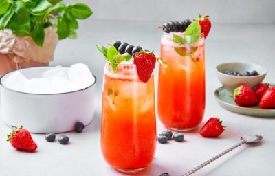 Twee mocktails staan op het aanrecht, klaar om te drinken. Hij heeft een mooie rode kleur door de aardbeien, het glaasje is afgewerkt met ijsblokjes, takje munt, aardbei aan het glas en een spiesje met blauwe bessen opgeprikt.