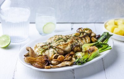 Ovengebakken zeeduivel ligt op een groot wit bord, geserveerd met gegrilde paksoi en champignons. Het gerechtje wordt geserveerd met gekookte aardappelen. Bovenaan staat ook ijskoud water met limoenschijfjes. 