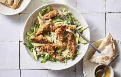 Er staat een diep bord op het aanrecht, gevuld met meerdere slasoorten en krokant gebakken leverreepjes. De mosterdressing staat er langs om zelf toe te voegen. 