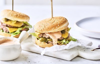 Twee heerlijke burgers liggen klaar op een marmere snijplank. Het vlees is verdeeld in twee dunne porties met de saus en gesmolten kaas er bovenop. De burgers worden recht gehouden door middel van een prikker.