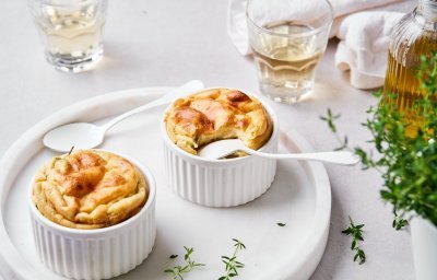 Twee soufflees staan op een wit bord klaargemaakt. In eentje is al een hapje genomen en zit het lepeltje er nog in. Het gerecht is afgewerkt met verse tijm. 