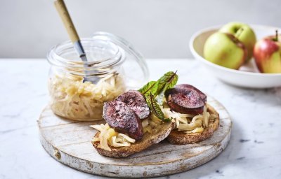 Twee toasten liggen op een houten serveerplank. Ze zijn belegt met chutney en gebakken niertjes. De overige chutney staat er langs in een glazen bokaal. 