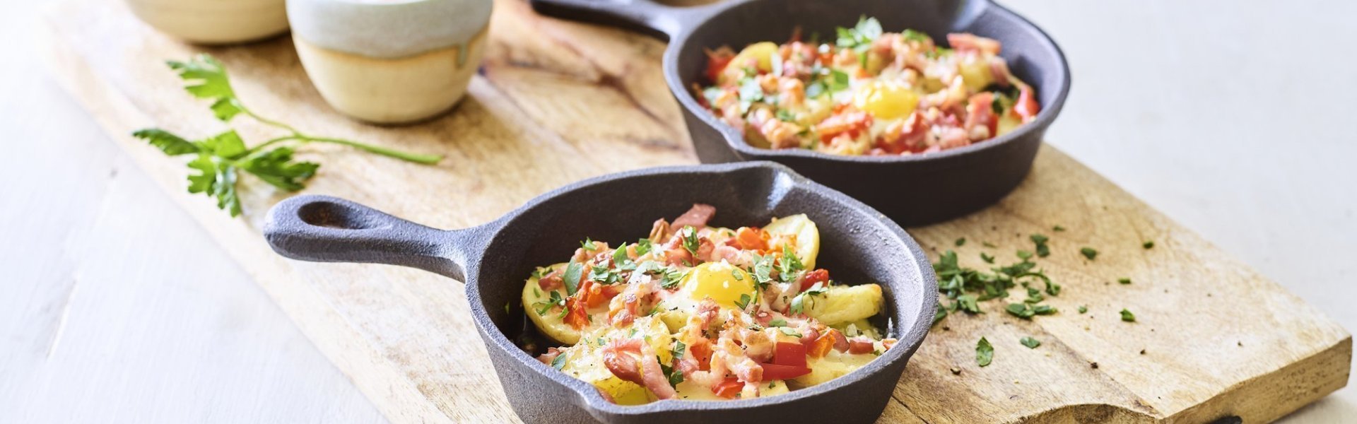 Twee gourmetpannetjes staan te sieren op een houten snijplank. Als bijgerechtjes hebben we een groene salade, opgelegde augurkjes en een cocktailsausje.